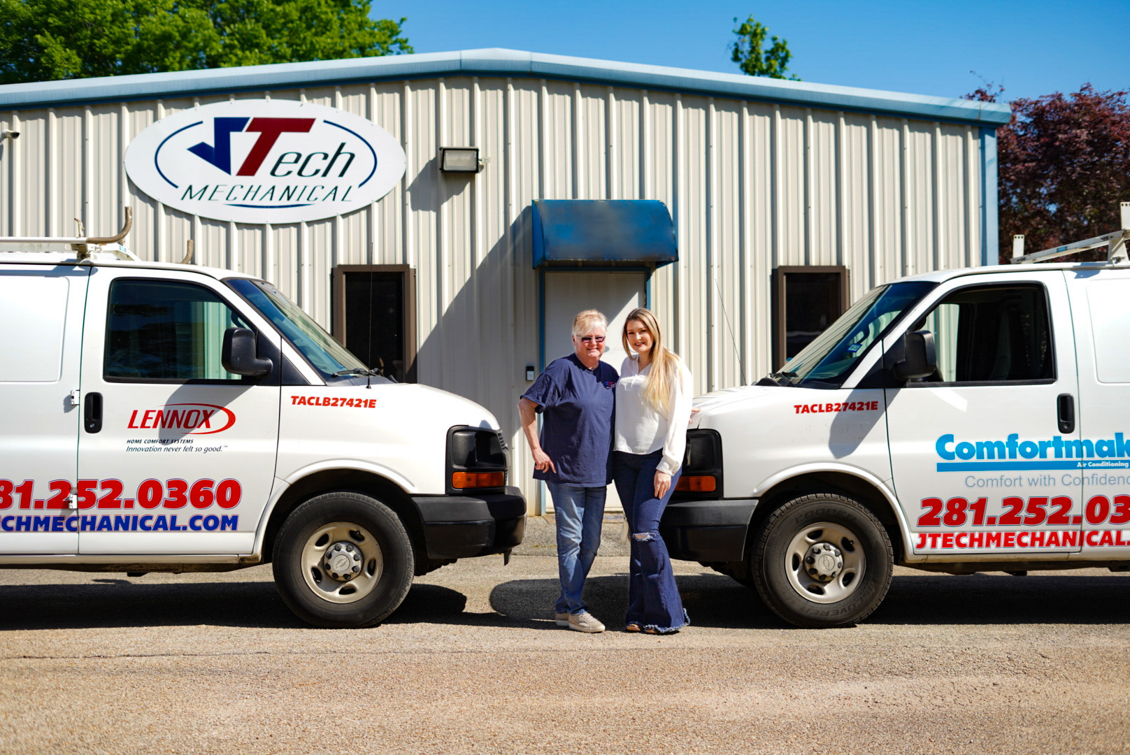 Melissa and Brittany standing in front of the JTech service trucks and a metal shop building.